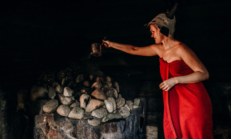 Woman pouring water on hot stones in smoke sauna