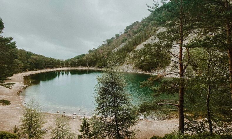 The unique green waters of Lochan Uaine lake surrounded by forest and mountains
