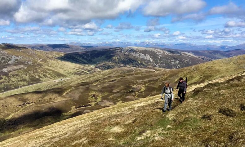 Two women hiking along a scenic mountain trail in Glenshee, Scotland