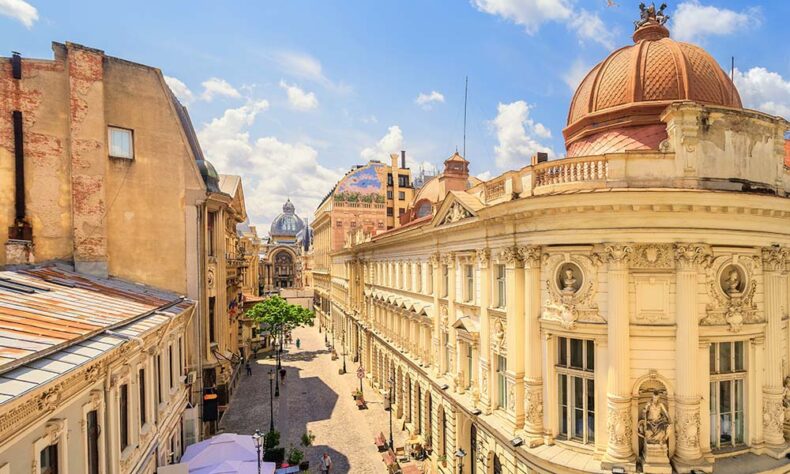 An elevated view looking down Lipscani Street in Bucharest, Romania, featuring the ornate classical architecture and copper dome of the National Bank of Romania on the right